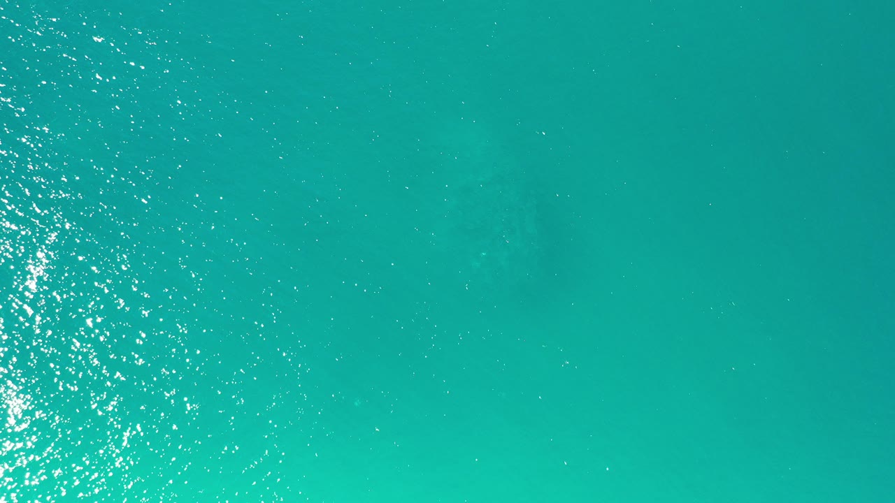 Top-down view of turquoise green sea water in Los Cabos, Mexico, with bright sun reflections along the left edge and no visible people.