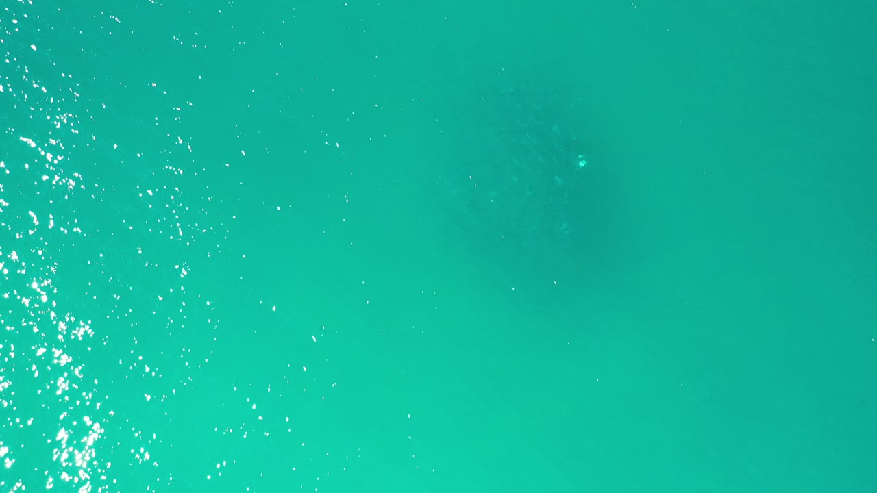 Overhead view of turquoise open water in Los Cabos, Mexico, with scattered white sun reflections near the left edge and no visible people.