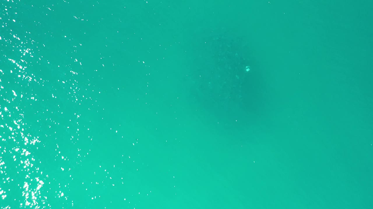 Turquoise open water in Los Cabos, Mexico, with a dense vertical strip of sun sparkle crossing the frame and no visible people.