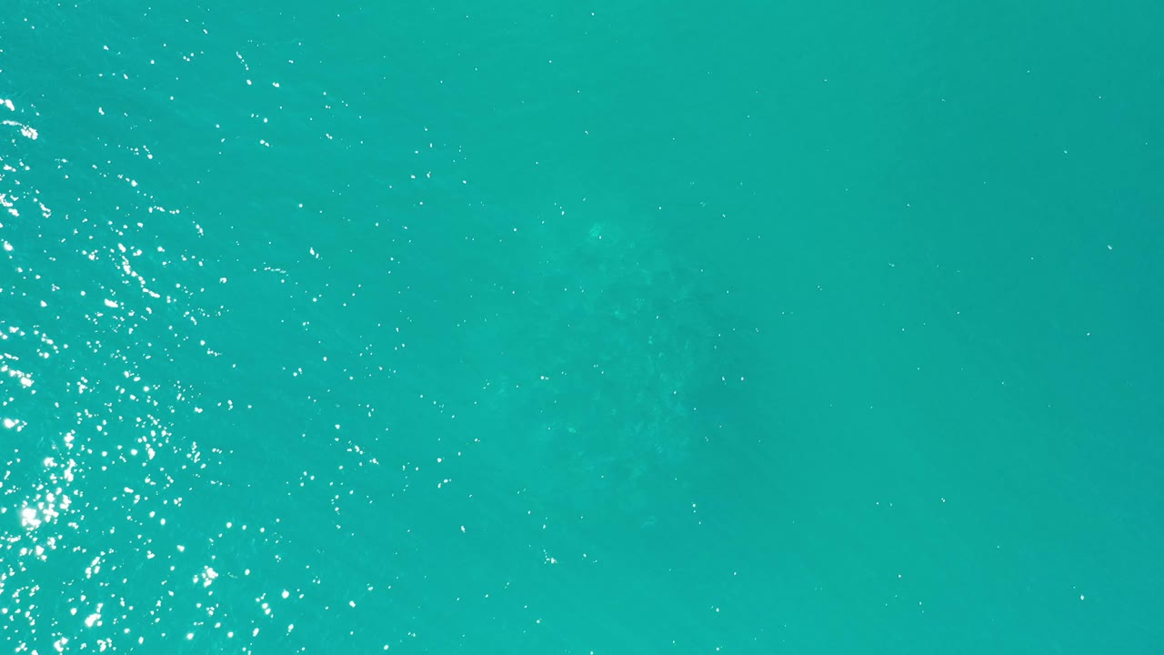Turquoise water in Los Cabos shows a narrow column of sun sparkle near the center, faint darker areas below the surface, and no visible people.