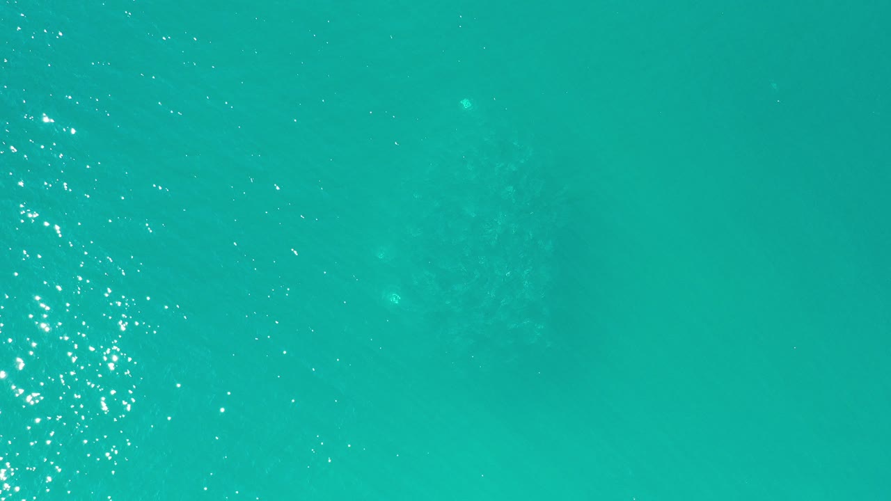 Aerial view of turquoise ocean water in Los Cabos, Mexico, with concentrated sun sparkle near the left side and no visible people.