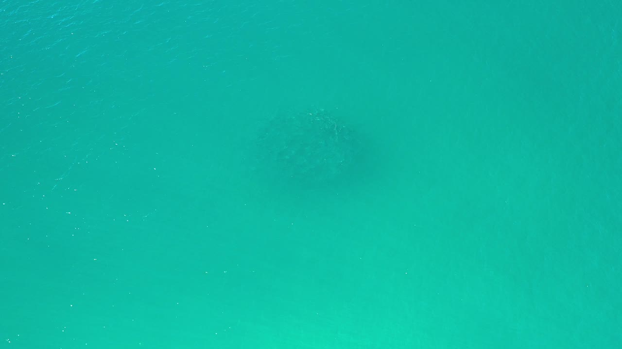 Overhead view of turquoise ocean water in Los Cabos, Mexico, with faint darker shapes under the surface and no visible people.