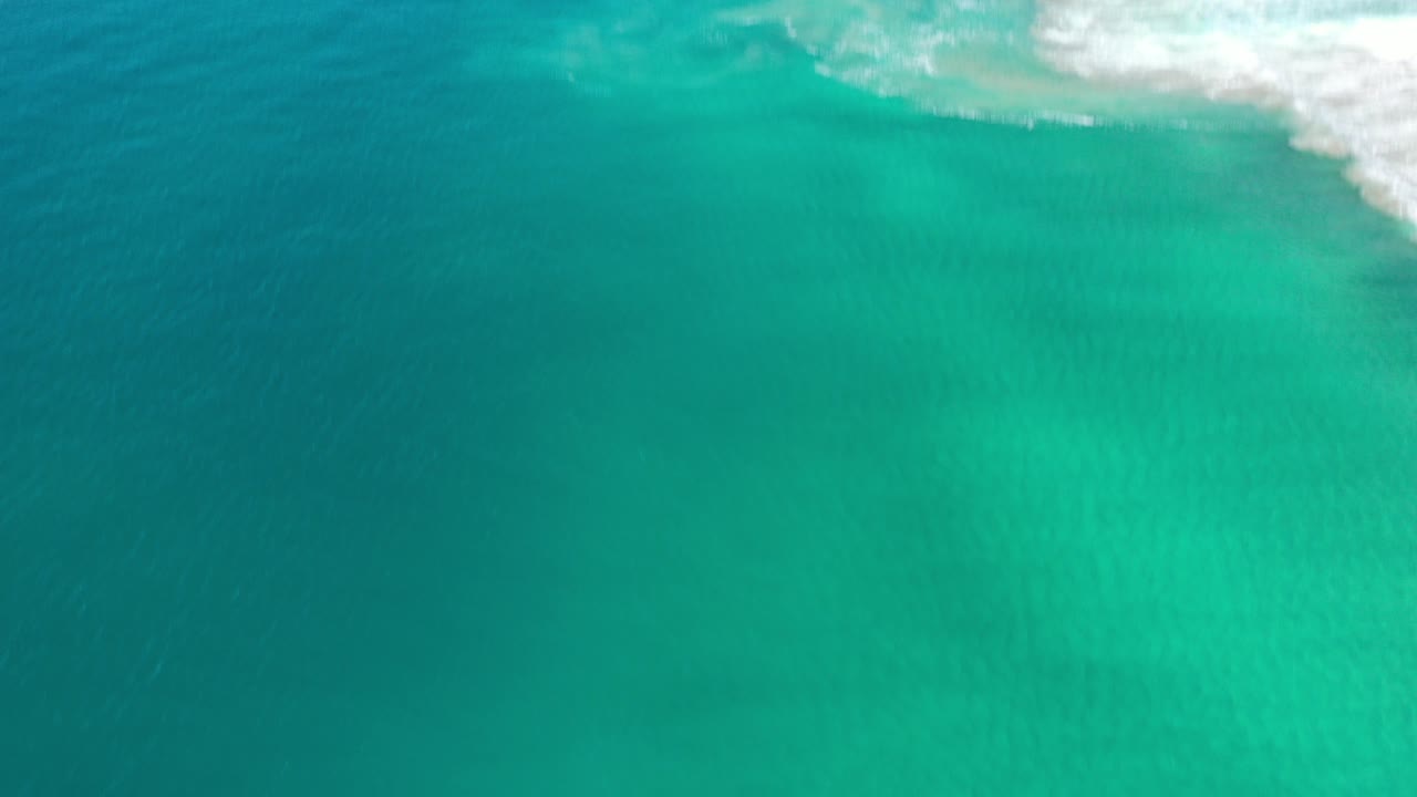 Aerial view of turquoise ocean water and white surf near shore