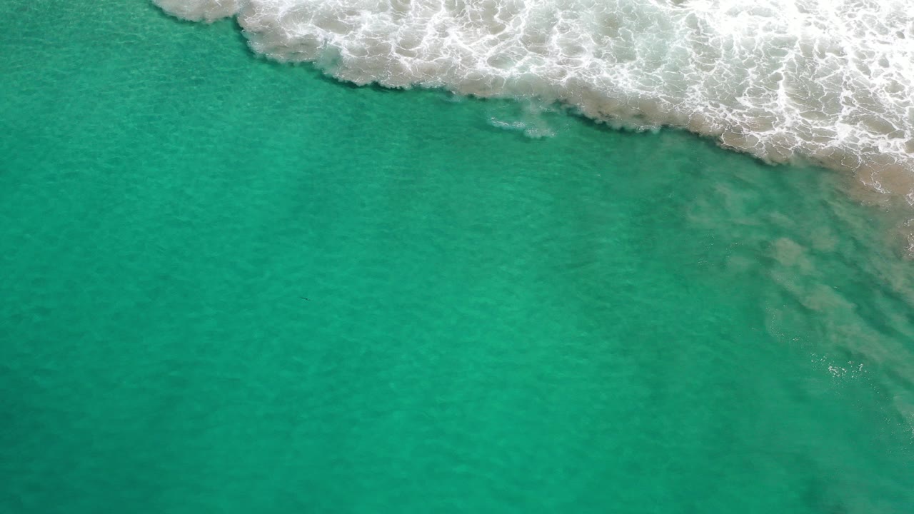 Overhead view of green sea water in Los Cabos, Mexico, with white foamy surf entering across the upper edge and no visible people.