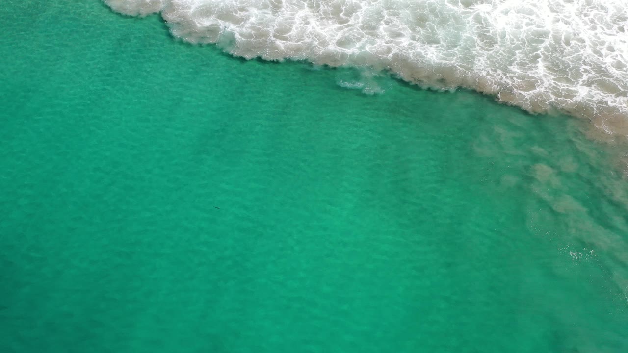 Foamy surf crosses the top over clear green sea water.
