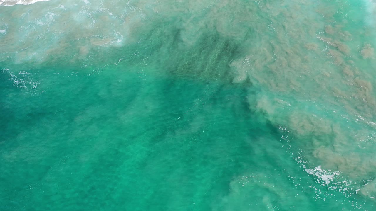 Steep overhead view of turquoise water in Los Cabos, Mexico, with the seabed visible below a thin line of white foam and no visible people.