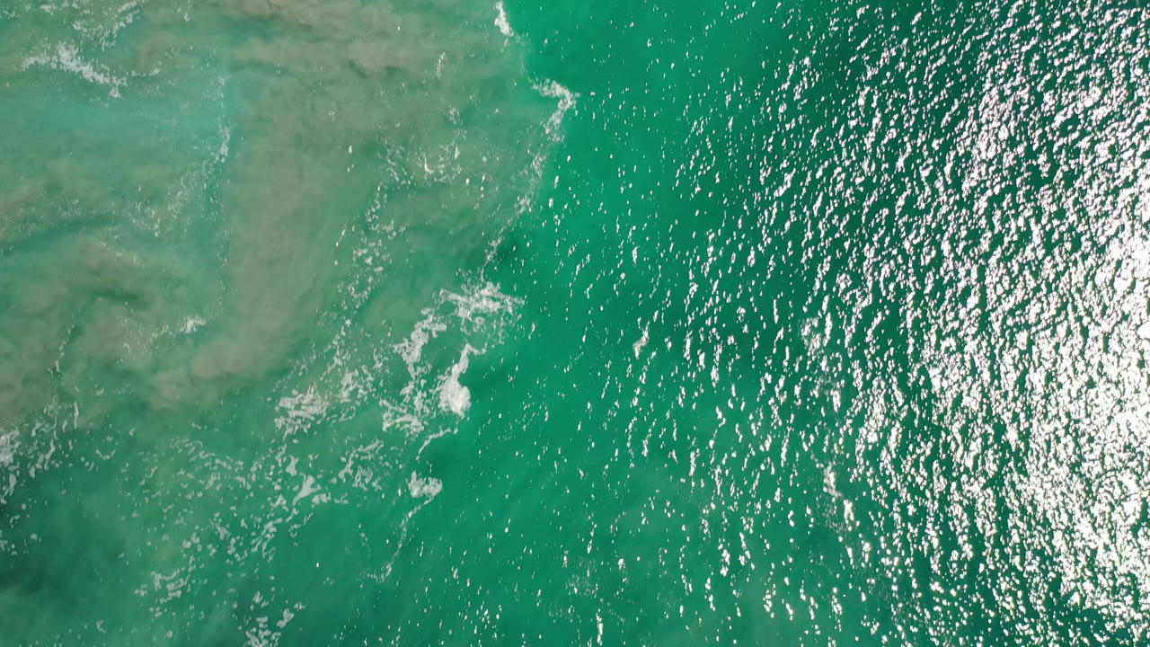 Green tropical water with bright ripples and faint white wave lines.