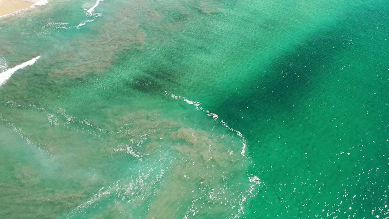 Turquoise coastal water with a diagonal white wave line and sand near the top.