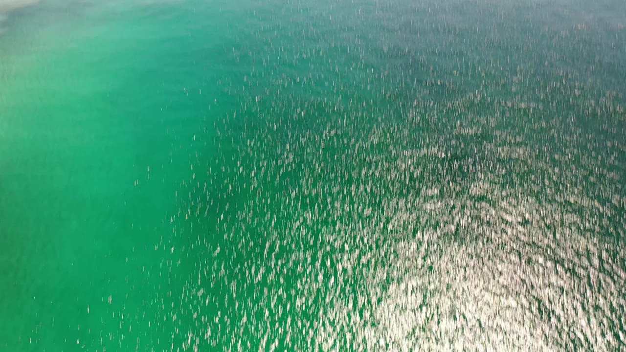 Overhead Los Cabos sea surface with a broad bright reflection near the lower center, darker water above, and no visible people.