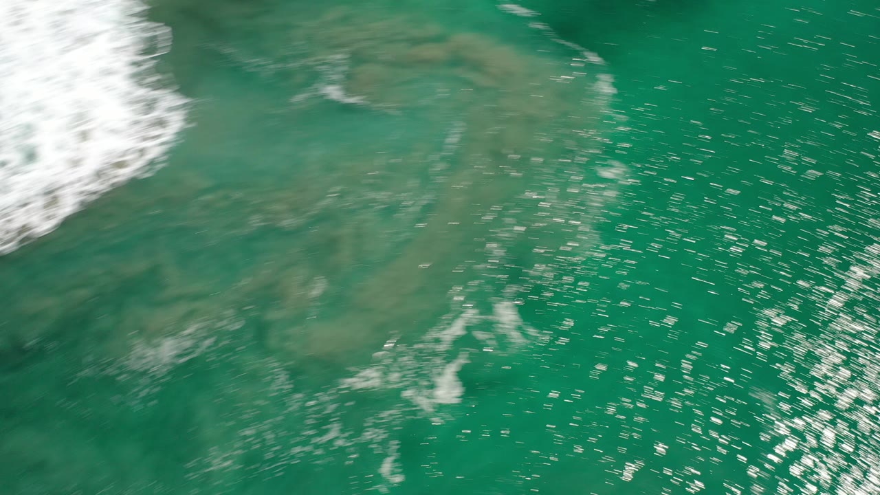 Turquoise ocean seen from above with white surf at the edge.