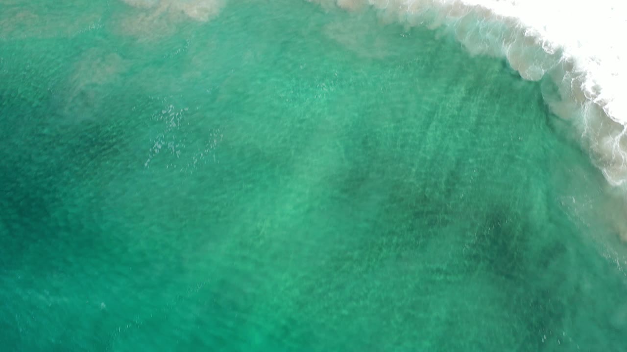 Clear turquoise water with surf foam at the upper right corner.