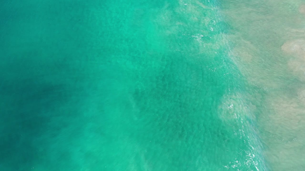 Overhead view of green-blue coastal water in Los Cabos, Mexico, with faint sand patches under the surface and no visible people.
