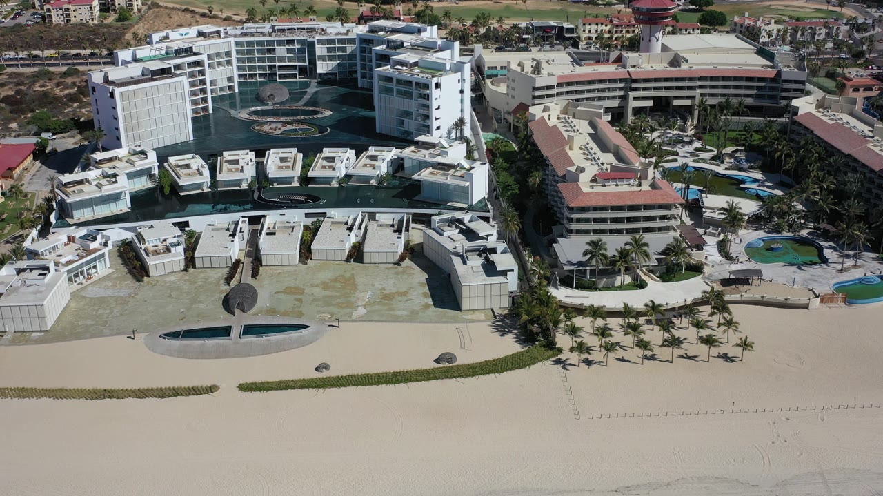 Beachfront resort buildings with palms and hillside background