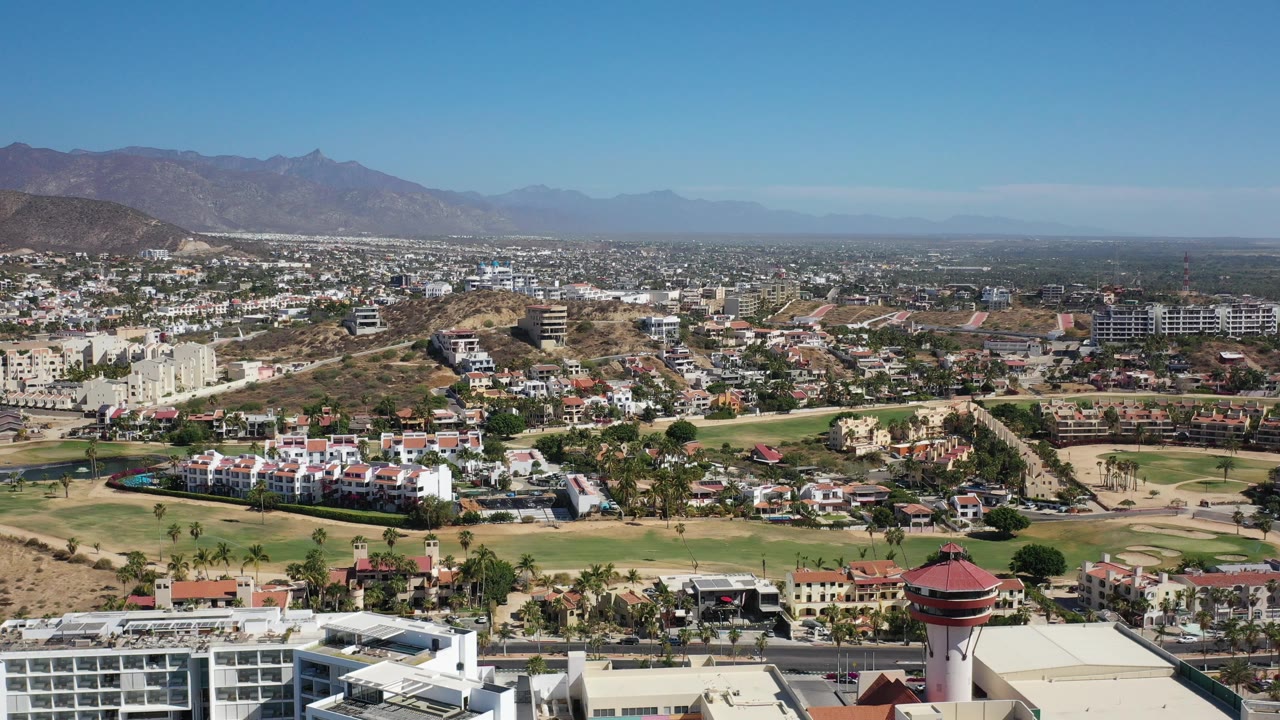 Wide aerial view over green parkland, buildings, hills, and mountains.