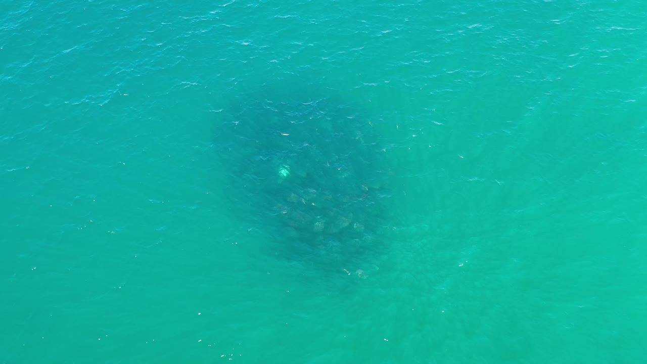 Overhead Los Cabos water view with the dark submerged patch slightly clearer under blue-green ripples and no visible people.