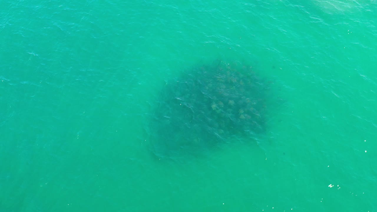 Turquoise water seen from above with a faint dark patch below the surface.
