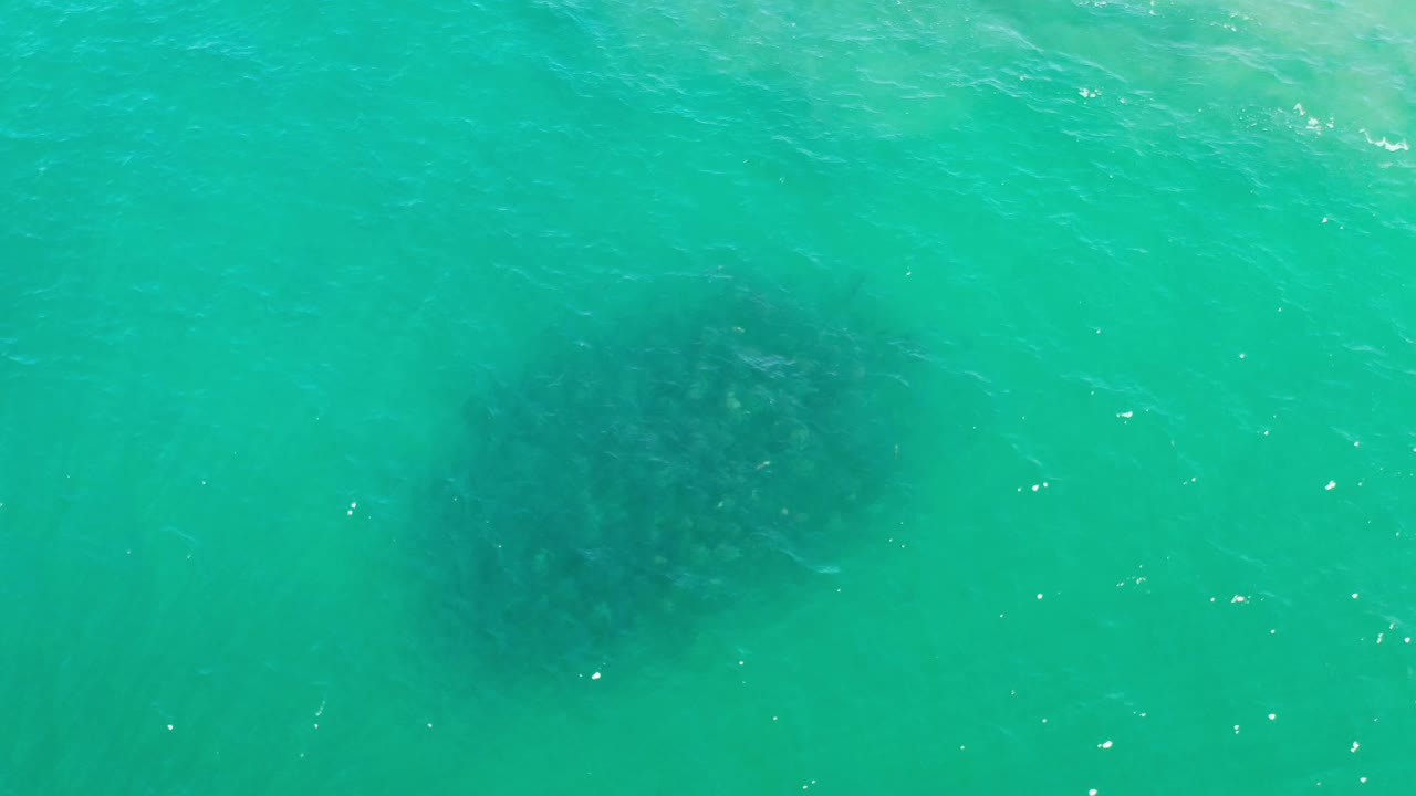 Los Cabos water appears bright turquoise with a darker underwater patch near the lower-left area and scattered white glints, with no visible people.