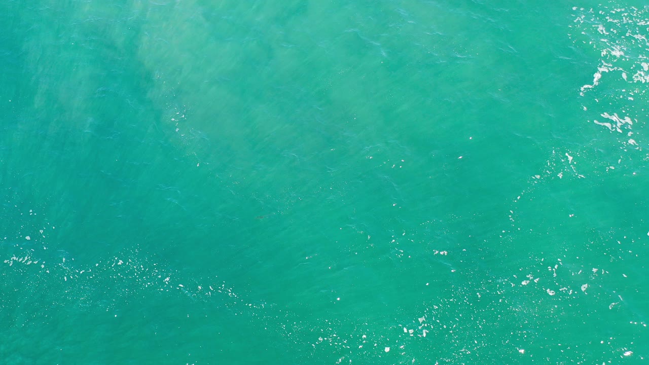 Top-down view of blue-green ocean water in Los Cabos, Mexico, with faint ripples, scattered white highlights, and no visible people.