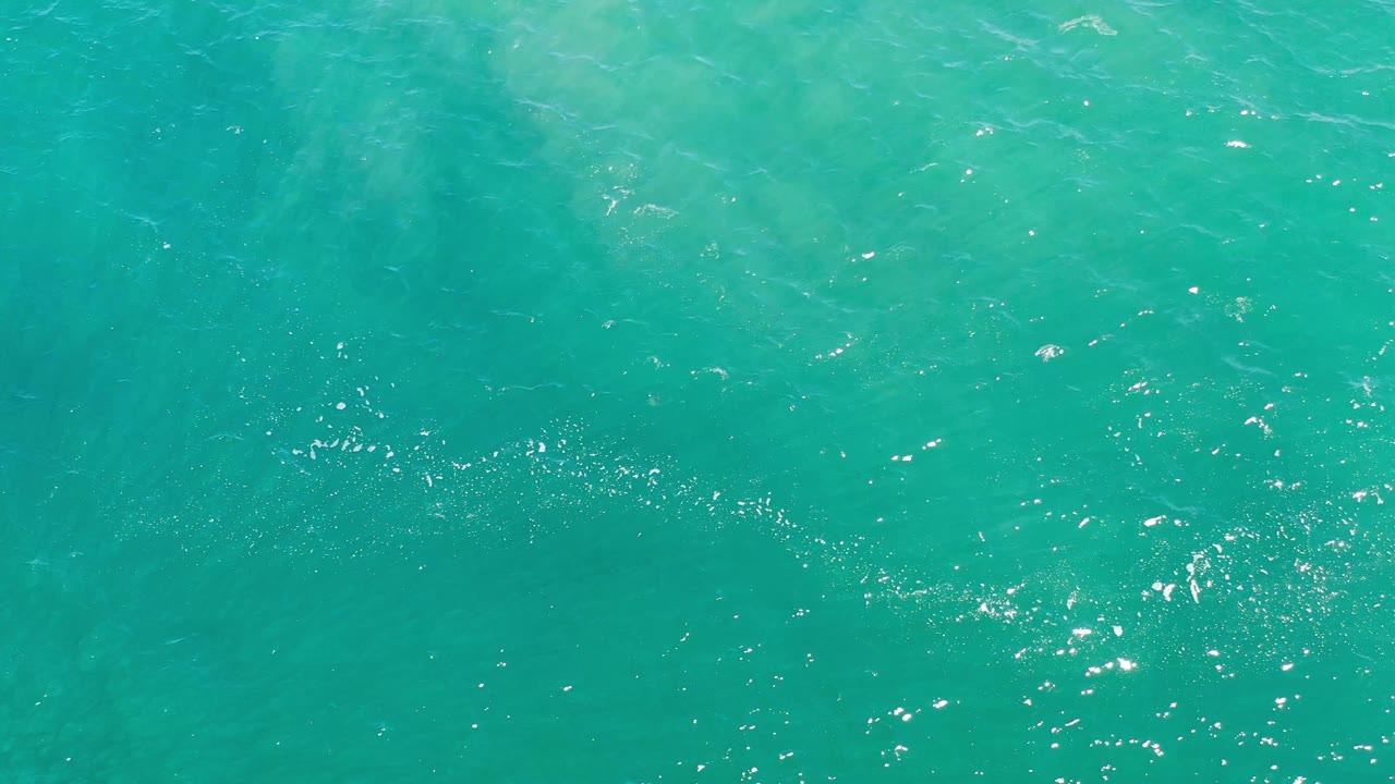 Overhead frame of Los Cabos sea water with faint darker underwater patches, light ripples, and no visible people or shoreline.