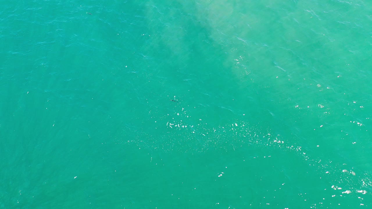 Overhead view of turquoise ocean surface in Los Cabos, Mexico, with faint darker patches under the water and no visible people.