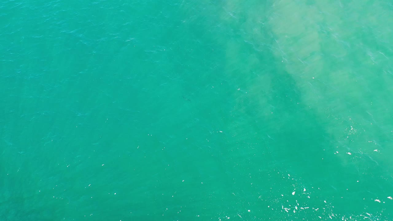 Overhead Los Cabos seawater frame with a wider pale clouded patch under the turquoise surface and no visible people.