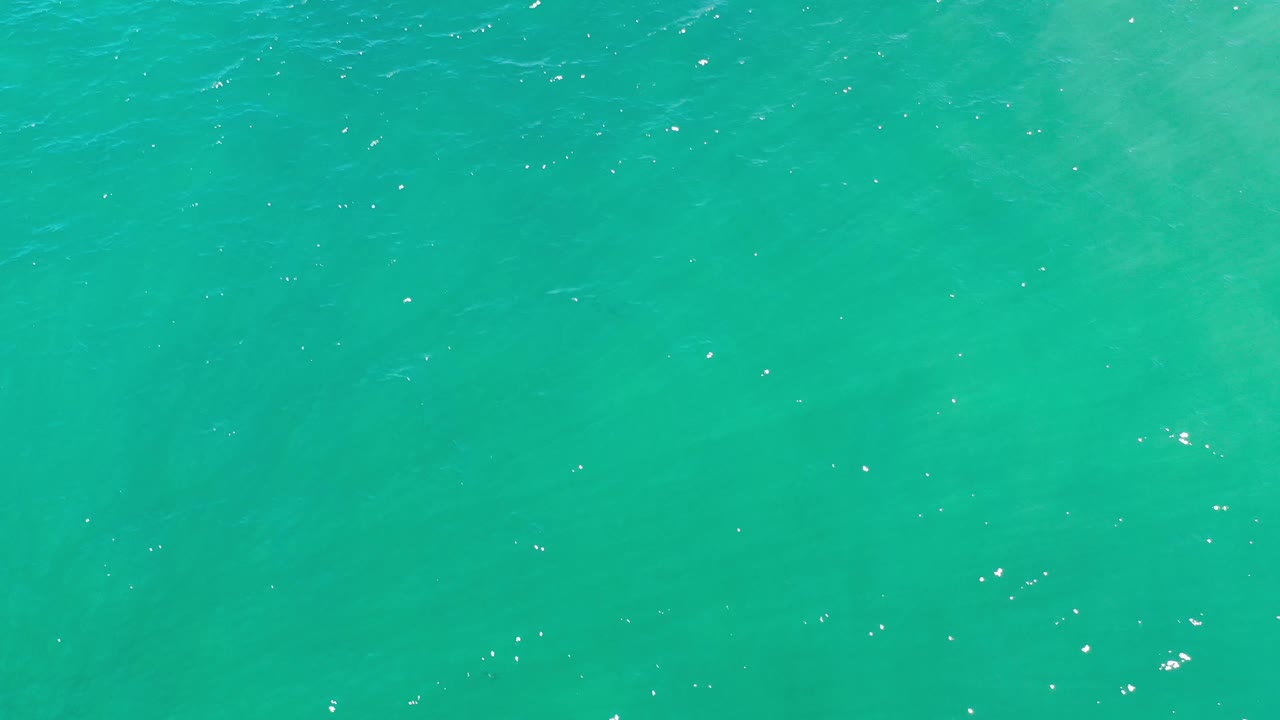 Aerial frame over Los Cabos ocean water, showing a broad green blue surface with faint darker areas below the ripples and no visible people.