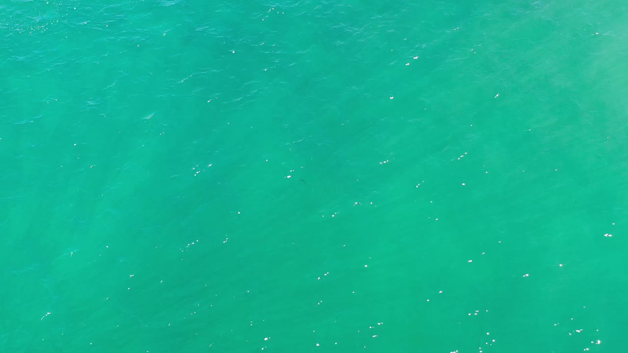 A blue-green water surface in Los Cabos, Mexico, shows faint rolling texture and sparse white glints, with no visible people.