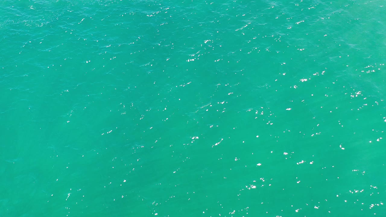 Light blue ocean water with scattered bright reflections.