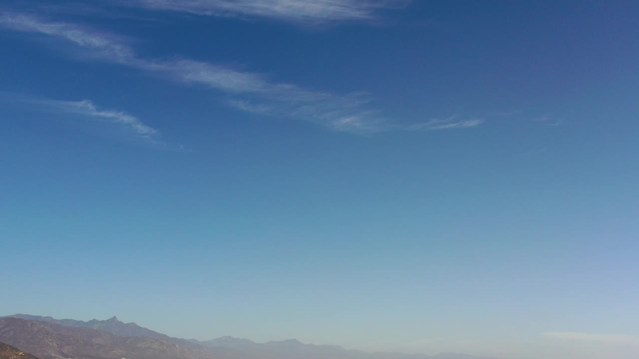 Opening Los Cabos, Mexico frame with mostly blue sky, thin high clouds, a low mountain ridge along the bottom edge, and no visible people.