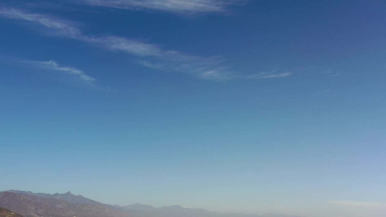 Second frame shows a broad blue sky over hazy Los Cabos mountain ridges, with the land still held low in frame and no visible people.