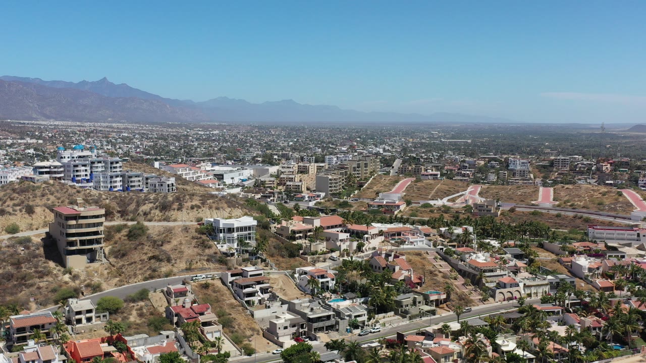 Aerial view of hillside homes, valley buildings, and distant mountains under clear sky.