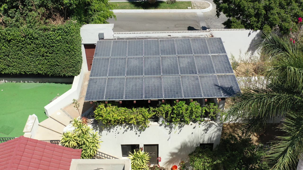 Aerial view of a white house with a dark solar-panel roof and green yard areas.
