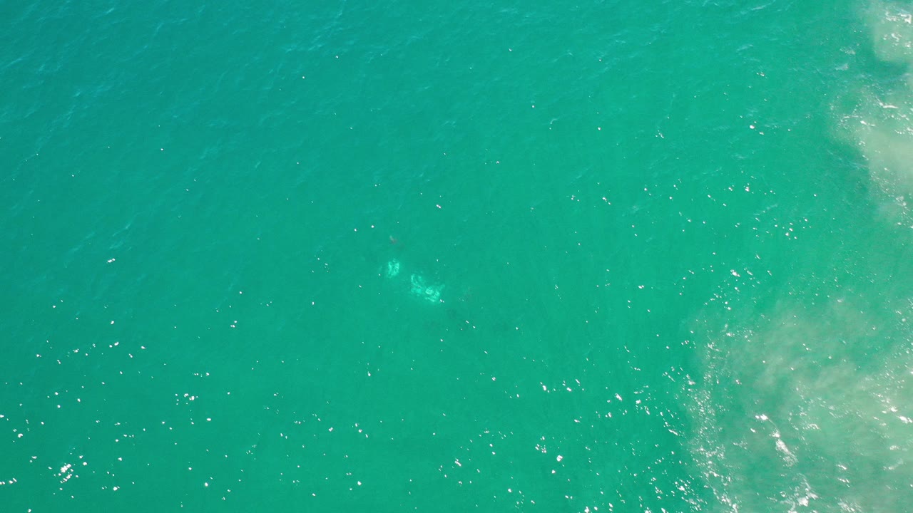 Top-down view of turquoise ocean with sun flecks and faint foam.