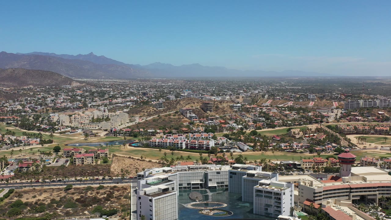 Sunlit aerial cityscape with foreground buildings and distant mountains.