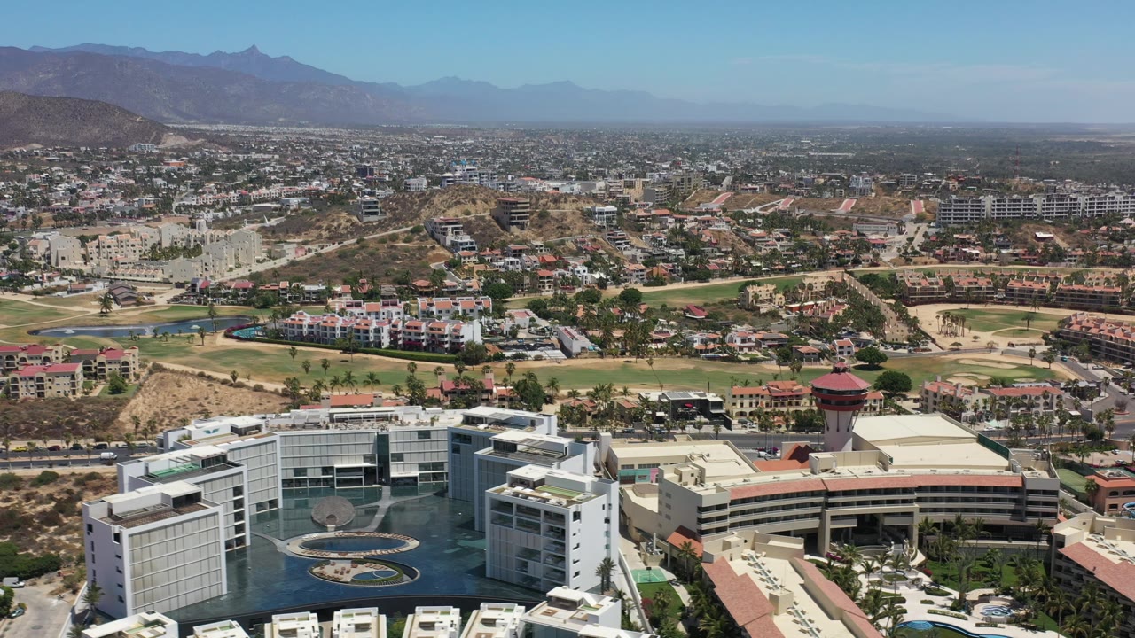High aerial view of a resort district with pools, roads, dry hills, and mountains.