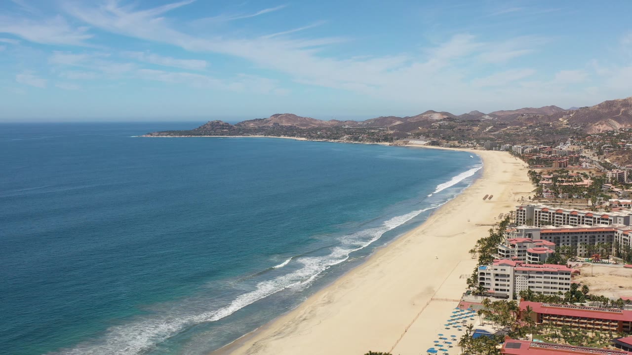 High view of a sandy beach curving around a blue bay below dry hills.