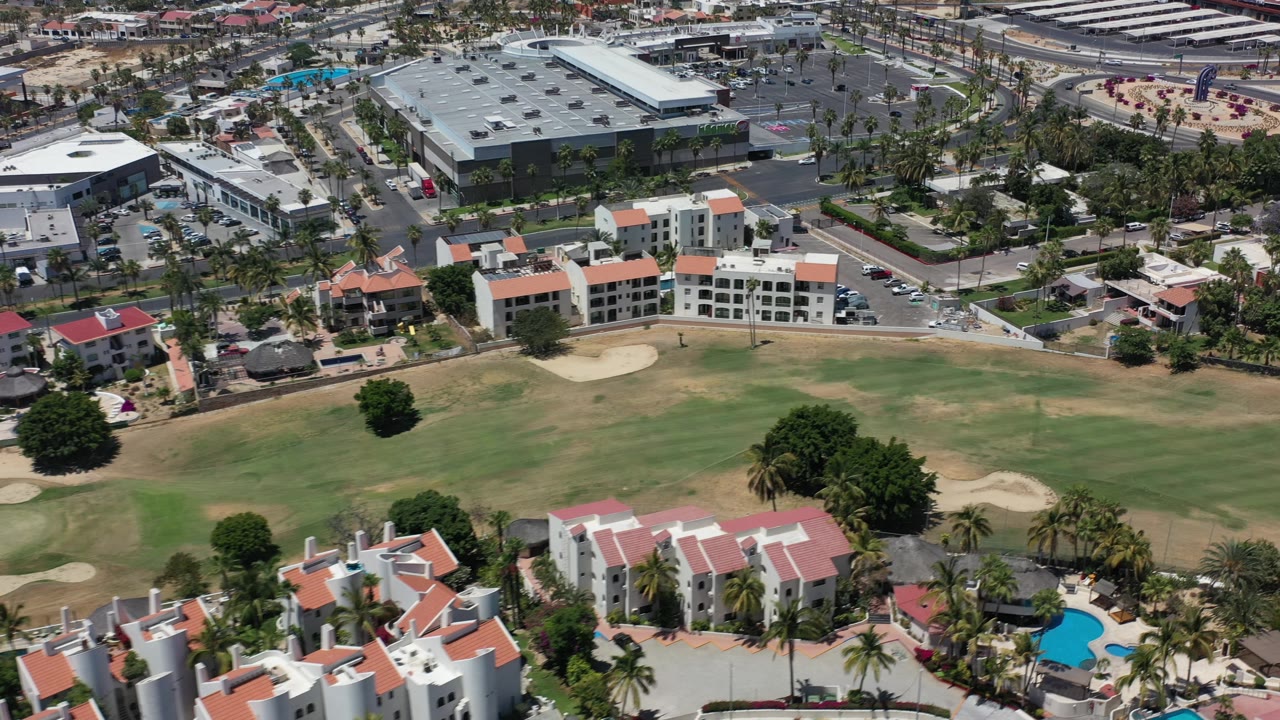 Birds-eye view of resort buildings beside a golf course and road network.