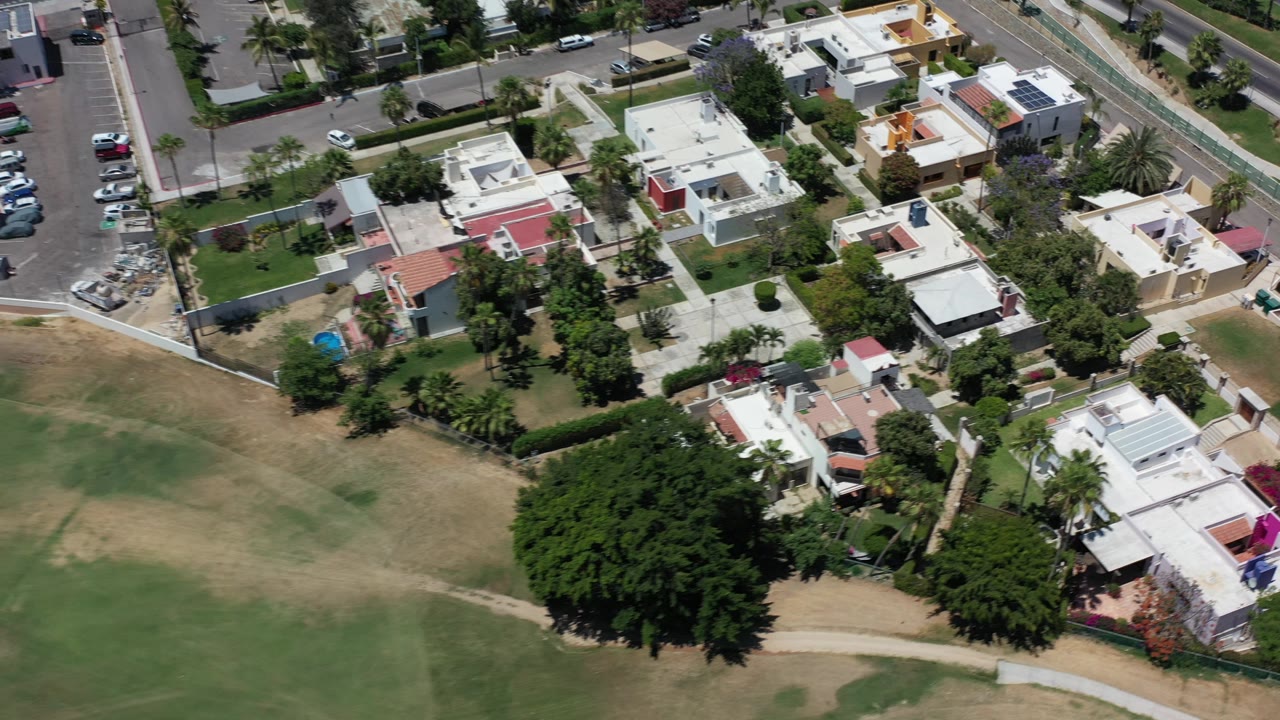 Aerial view of homes, a road, and a tree-lined field edge.