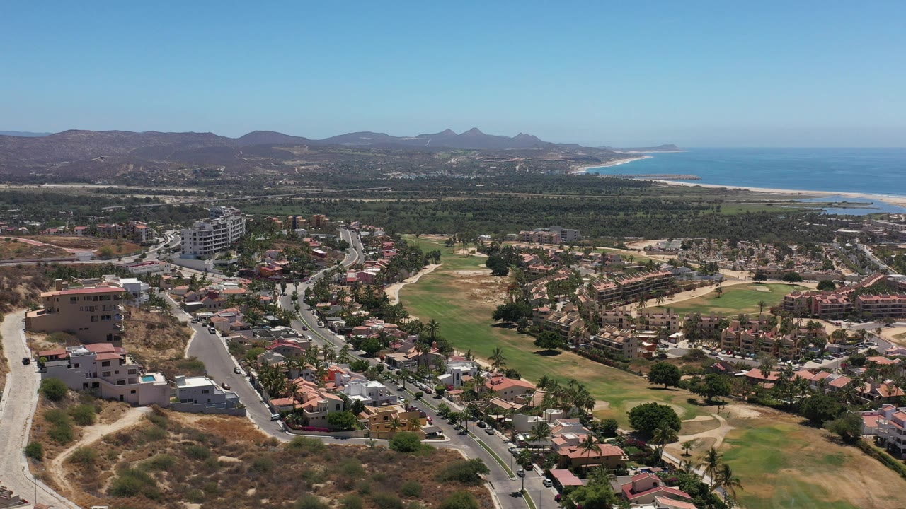 Aerial view of coastal neighborhoods, green lawns, hills, and ocean.