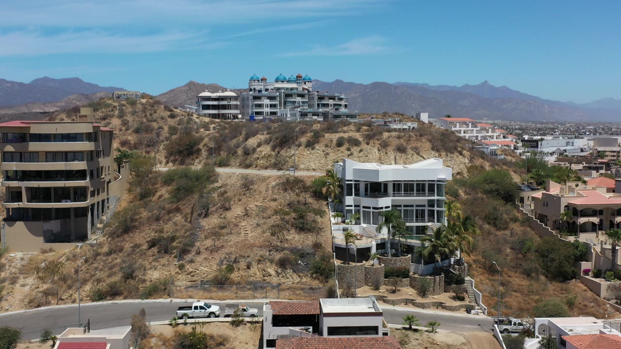 Modern houses on a dry hillside with roads and mountains behind.