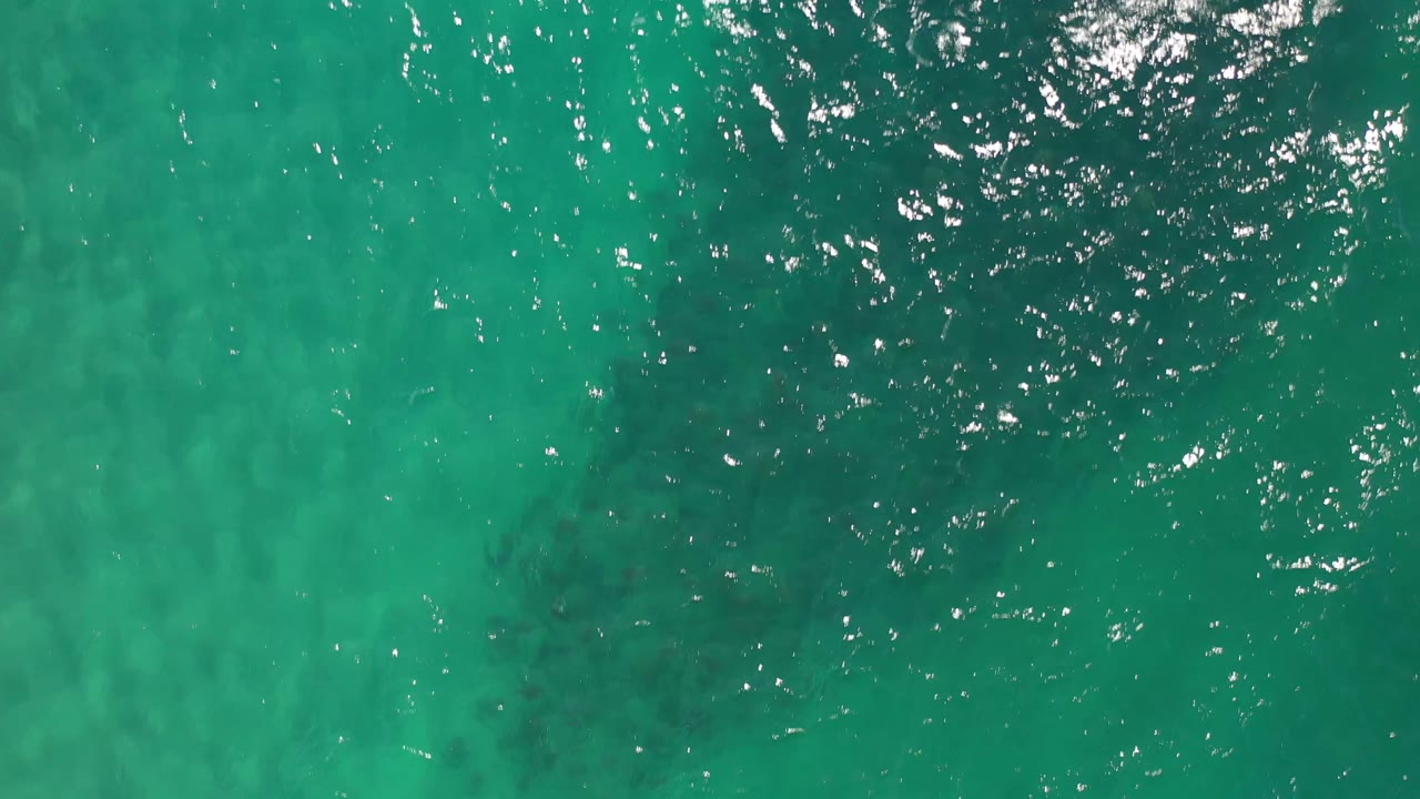 Turquoise ocean surface in Los Cabos, Mexico, seen from above with fine ripples, faint darker patches below the water, and no visible people.