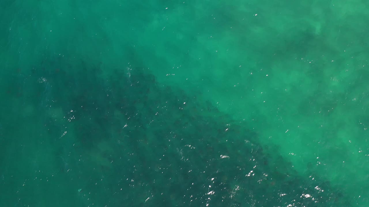 Turquoise green ocean surface in Los Cabos, Mexico, seen from above with faint ripples, cloudy underwater color variation, and no visible people.