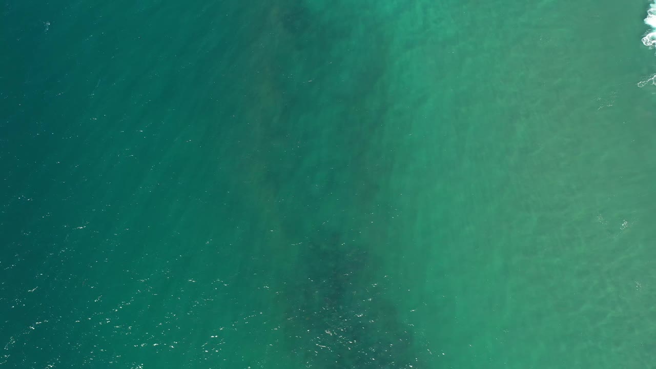 Green-blue Los Cabos ocean water seen from above, with a small white foam break near the top edge and no visible people.