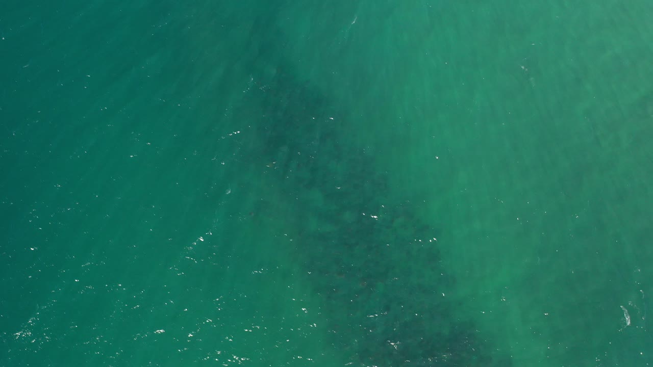 Top-down turquoise ocean with darker submerged patches