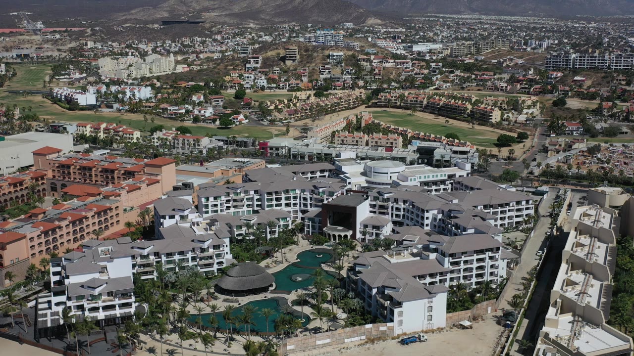 Wide aerial of a resort complex with pools and nearby residential development.