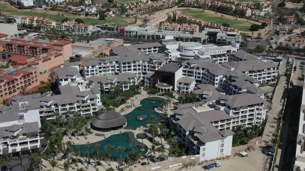 Aerial view of condo buildings, pools, palms, and nearby roads.