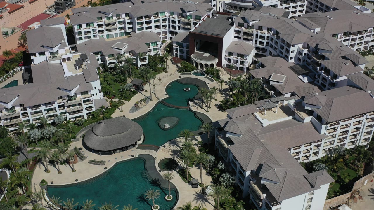 Overhead view of hotel buildings around turquoise pools and palm landscaping.