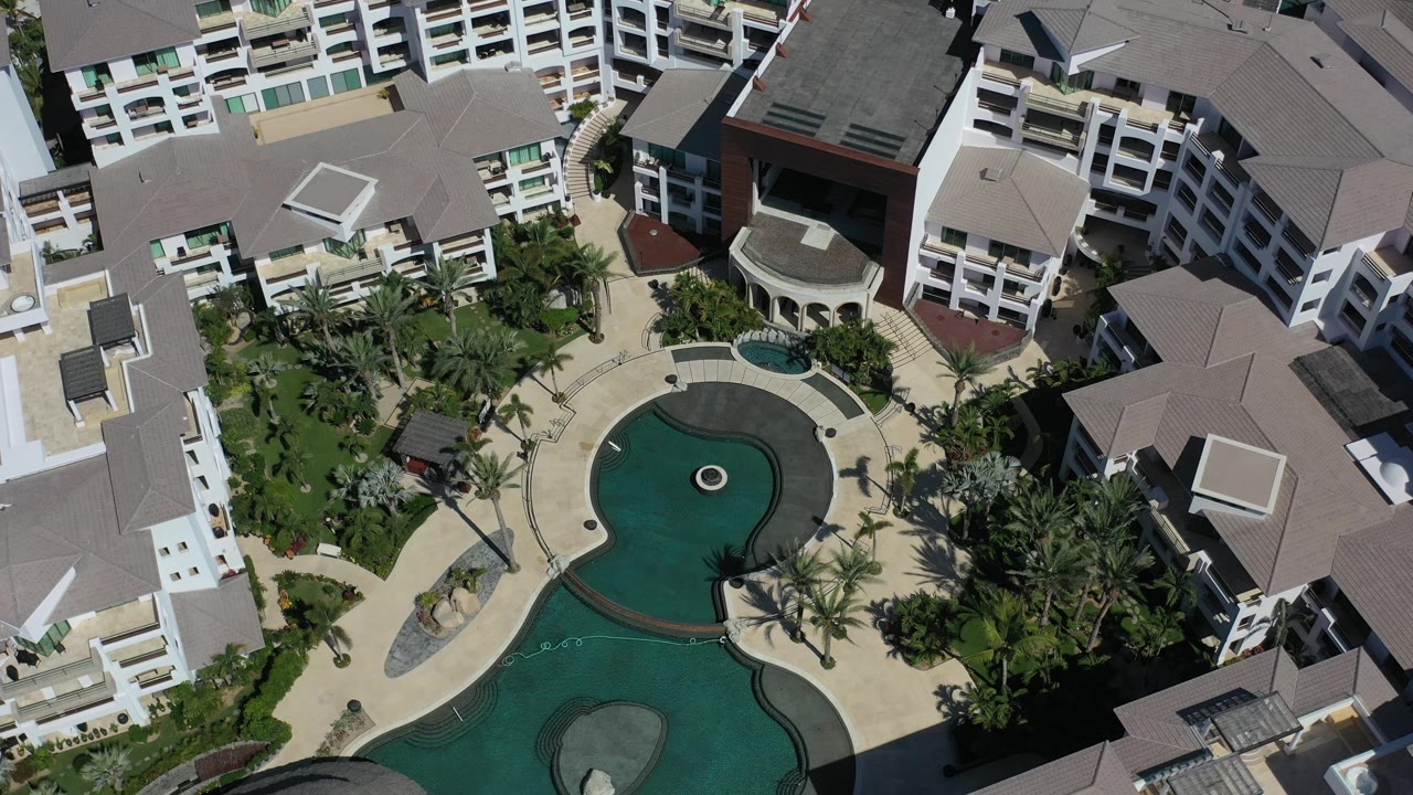 Drone view across resort pools, palm trees, and white hotel wings.