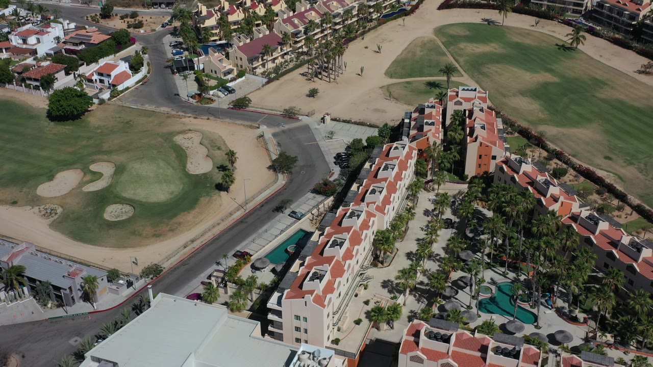Overhead view of golf greens, sand traps, roads, and red-roofed buildings.