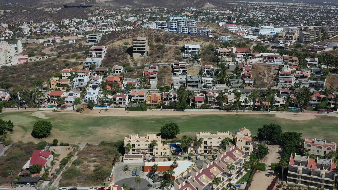 Aerial view of houses, streets, grass, trees, and dry hills.